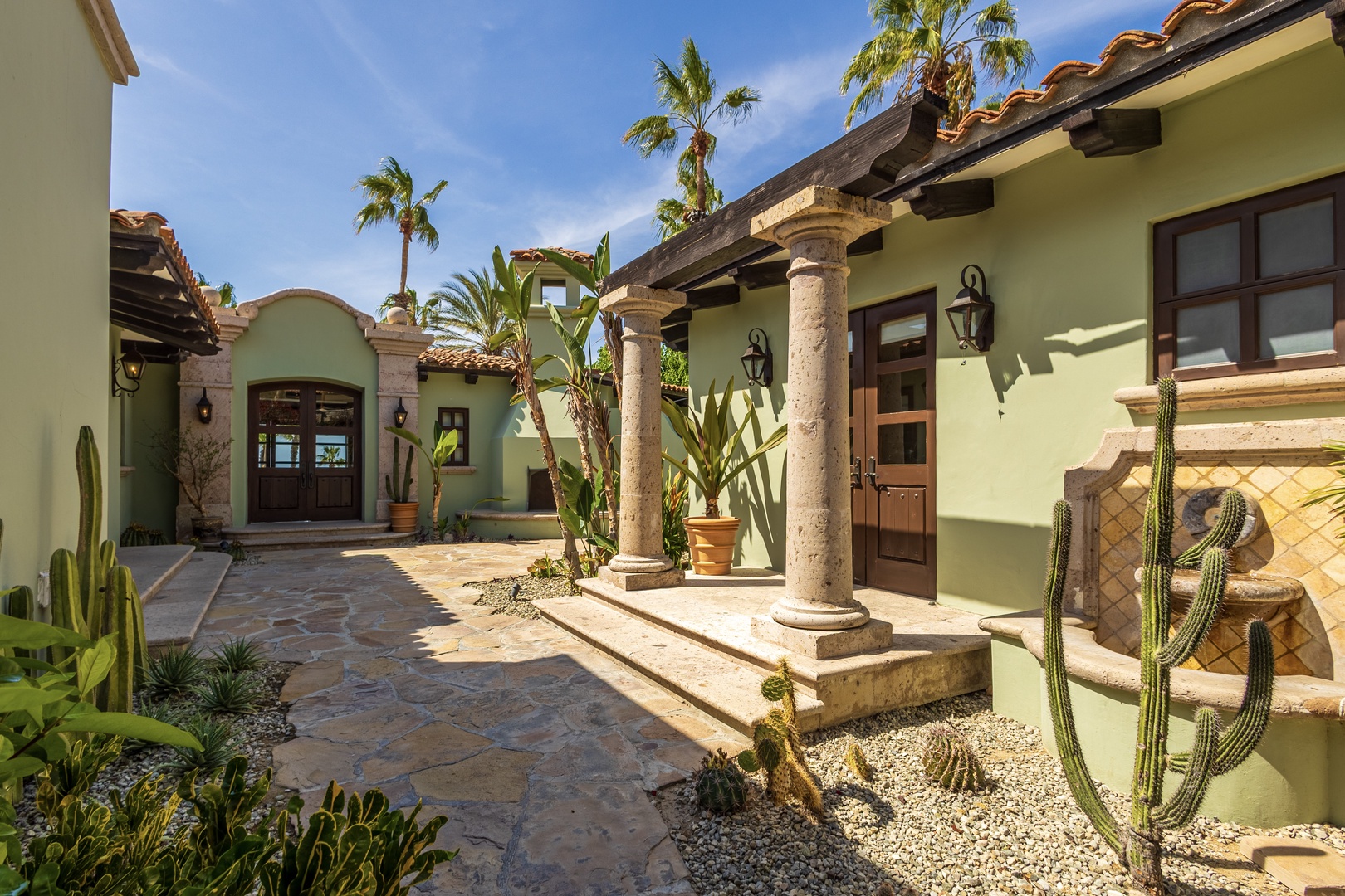 Beautiful hacienda-style entrance with stone columns and tropical landscaping welcomes guests to this desert oasis retreat.