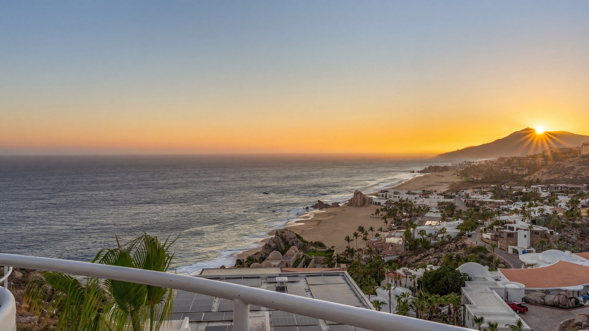 Golden sunset paints the sky over this stunning coastal vista, showcasing the pristine beach and charming neighborhood below.