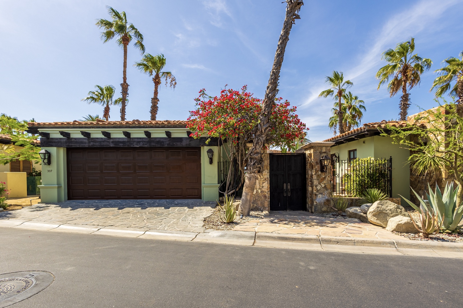 Tropical paradise awaits behind elegant stone entrance with vibrant bougainvillea and swaying palms creating perfect desert oasis setting.