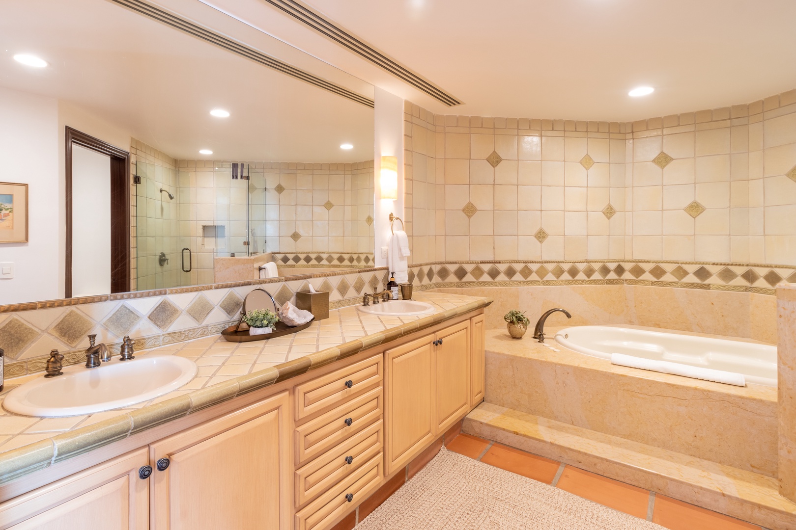 Unwind in your luxurious bathroom featuring dual sinks, a spacious soaking tub, and a separate glass-enclosed shower. Warm tiled accents and soft lighting create your personal spa retreat.