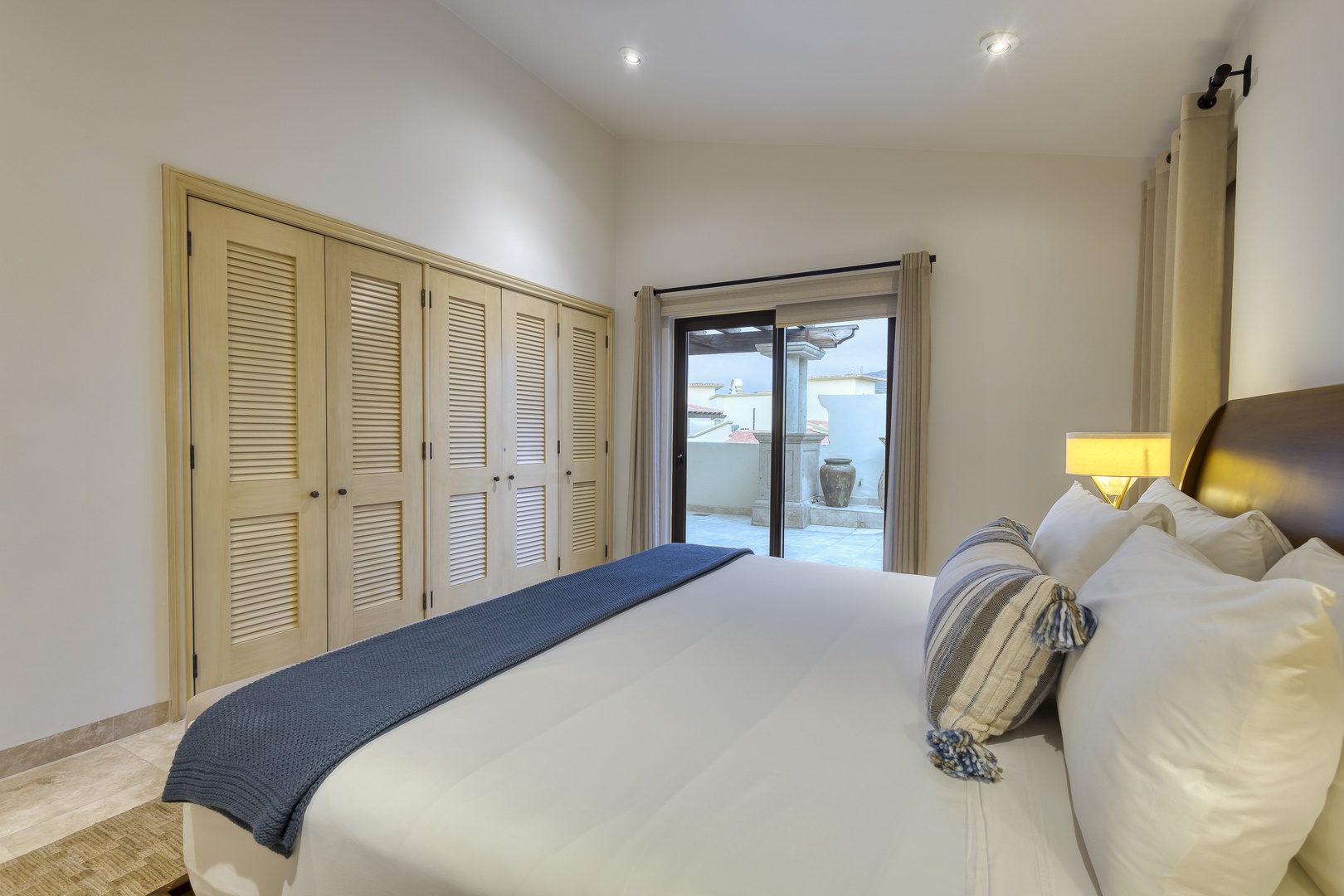 Sink into your plush king bed with coastal-inspired linens and decorative pillows, where soft lighting and a private patio invite you to unwind in comfort.