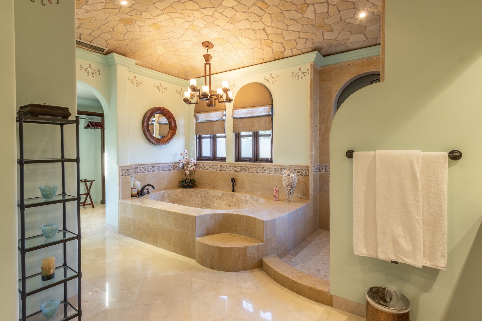 Sink into your spacious soaking tub beneath a stunning mosaic ceiling and warm chandelier glow. Fresh towels await as natural light filters through elegant arched windows.
