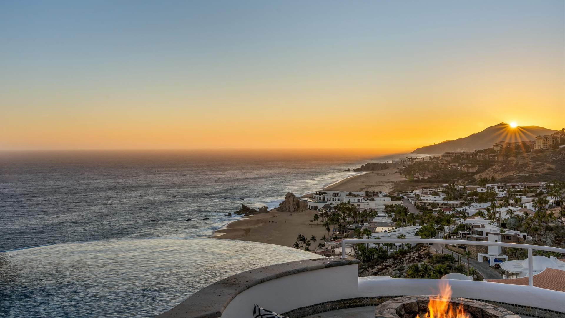 Stunning coastal sunset view overlooking white villa-dotted coastline and pristine beaches along the dramatic shoreline.