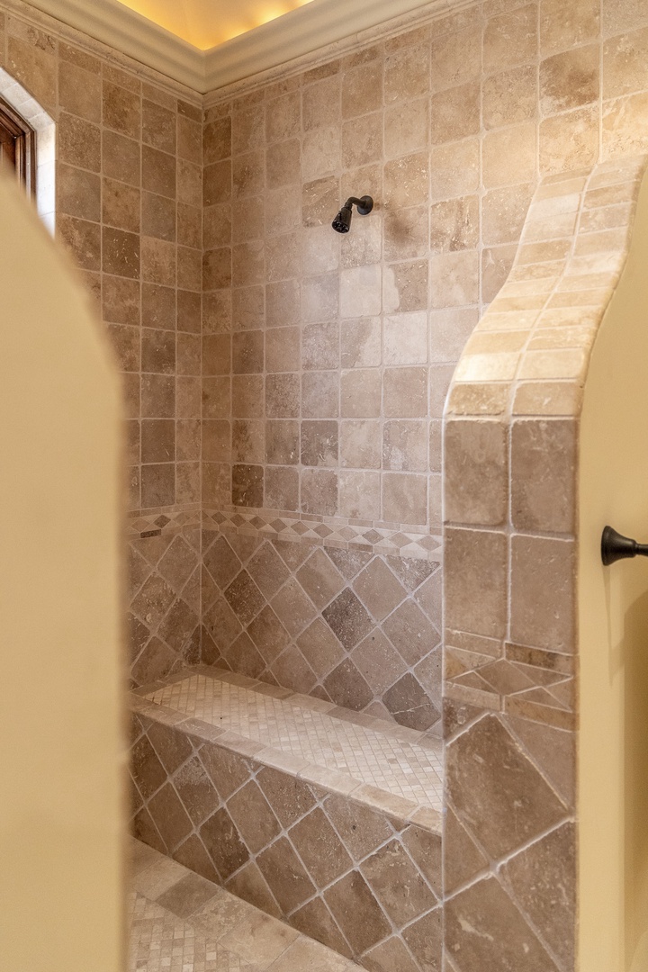 Step into your private spa-like retreat with a stunning stone walk-in shower featuring elegant tile work, built-in bench seating, and warm ambient lighting overhead for ultimate relaxation.