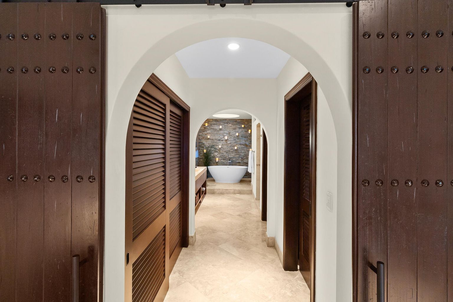 Handcrafted wooden doors open to a spa-like bathroom retreat. A stunning freestanding tub, warm stone accents, and modern elegance create your personal escape.