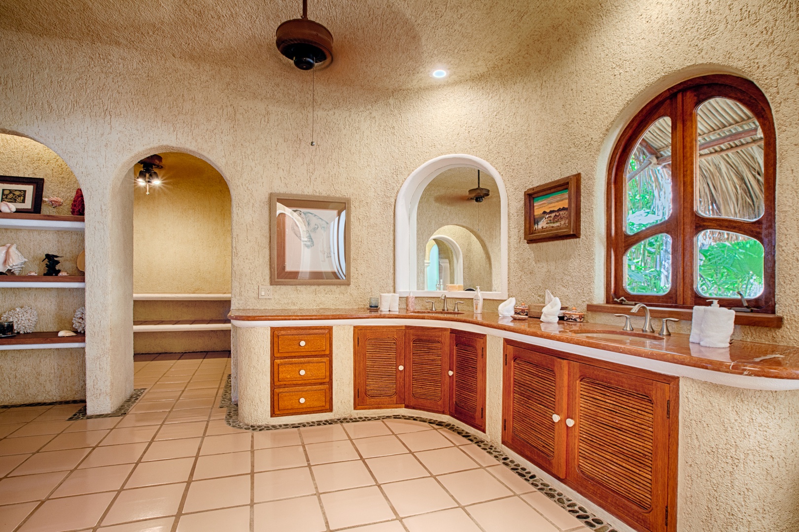 Unwind in your luxurious bathroom featuring handcrafted wood cabinetry, elegant archways, and natural light streaming through tropical garden views.