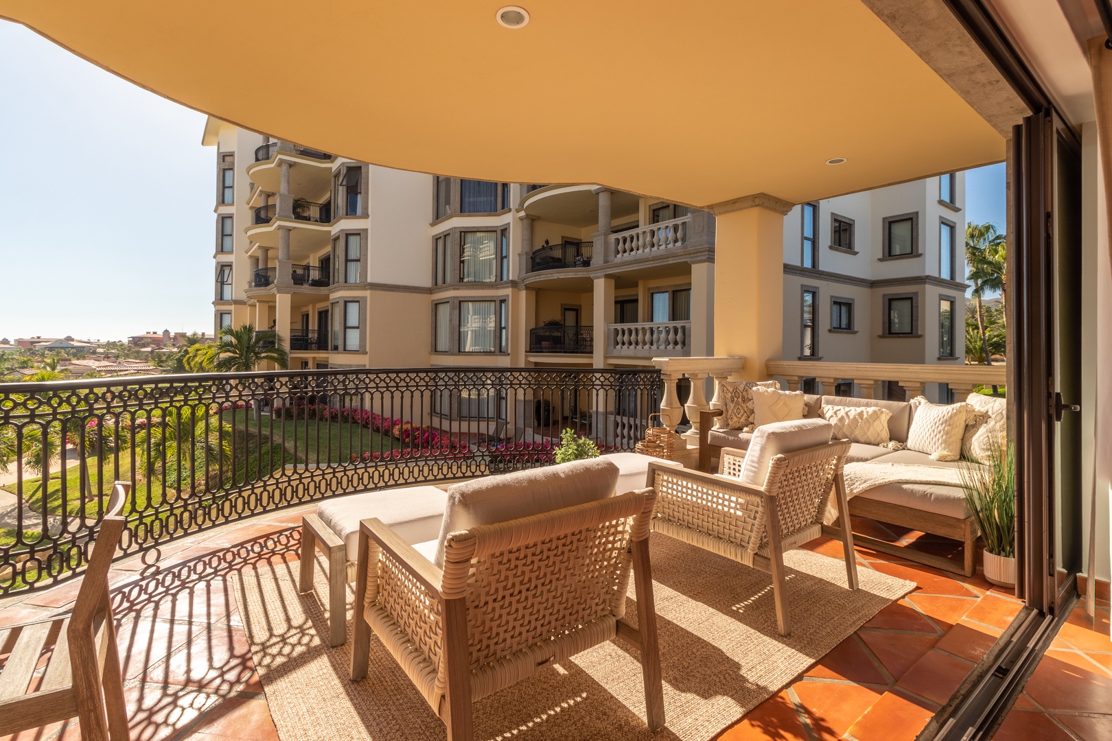 This spacious balcony offers comfortable seating with woven chairs and plush cushions, perfect for morning coffee or sunset relaxation. The terracotta tile floor adds warmth as you take in views of the resort's landscaped grounds and surroundings.