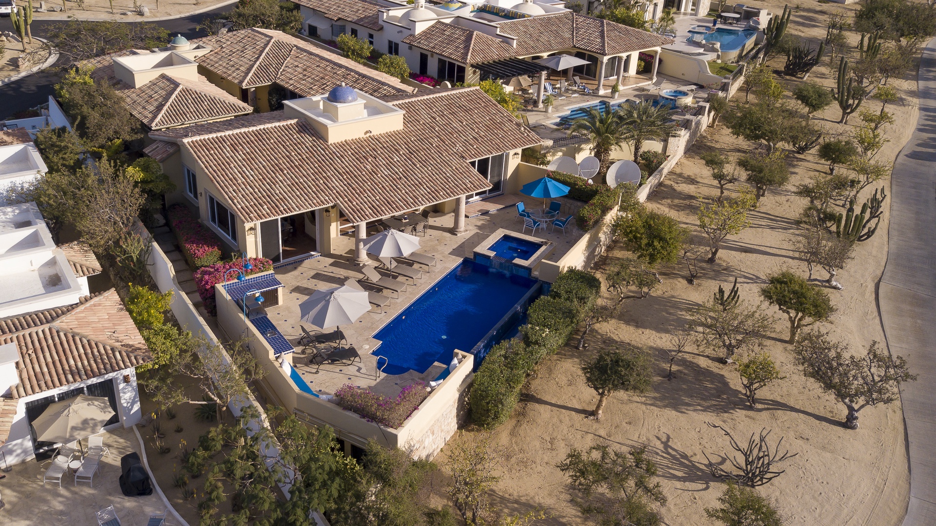 Aerial view of a luxury villa featuring a sparkling blue pool, terrace areas, and desert landscaping in a peaceful residential community.