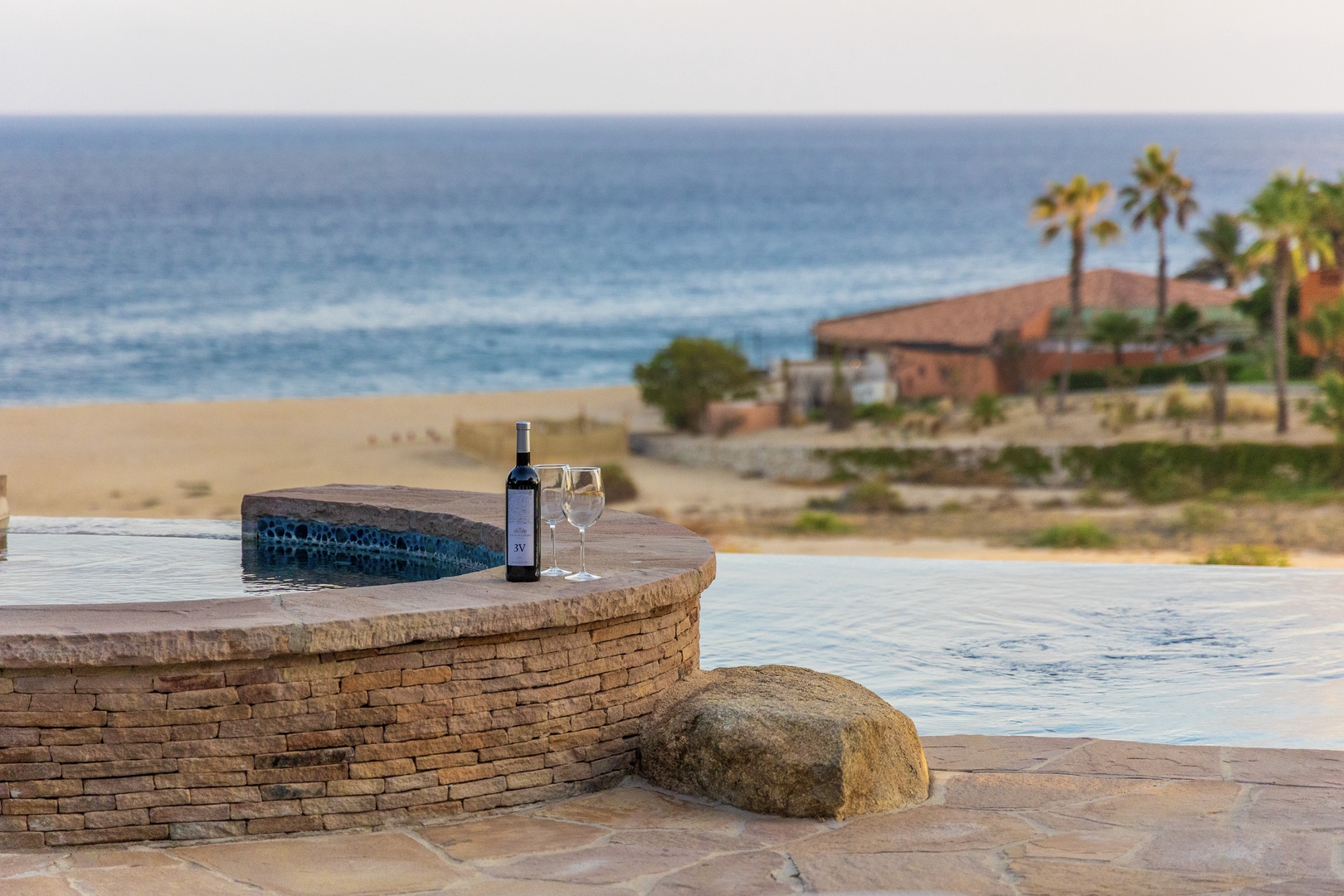 Beachfront property featuring an infinity pool, palm trees, and direct ocean access. The setting offers a tranquil coastal retreat with sandy beaches and scenic water views.