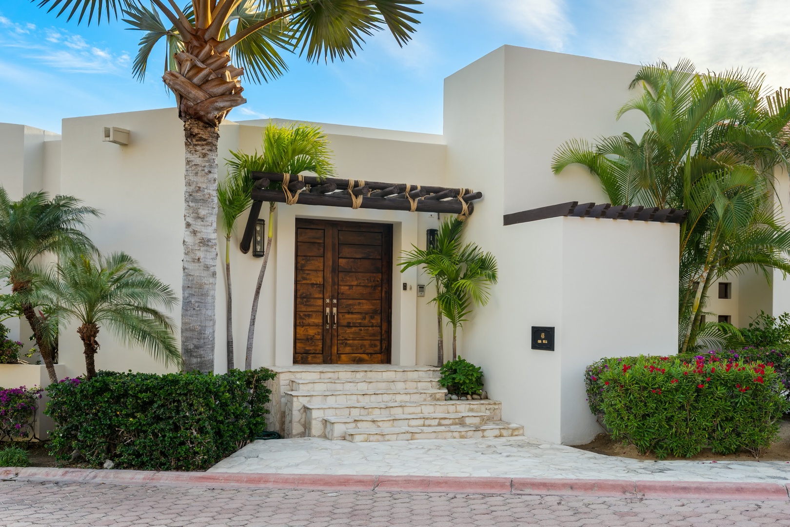Modern tropical villa with elegant wooden entrance doors and lush palm landscaping in a peaceful resort setting.