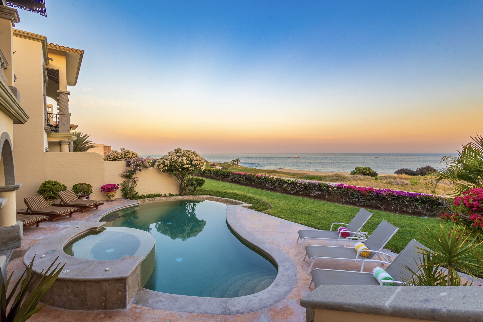 Beachfront property featuring a private pool, lush garden, and stunning ocean views at sunset, surrounded by vibrant tropical landscaping and coastal natural beauty.