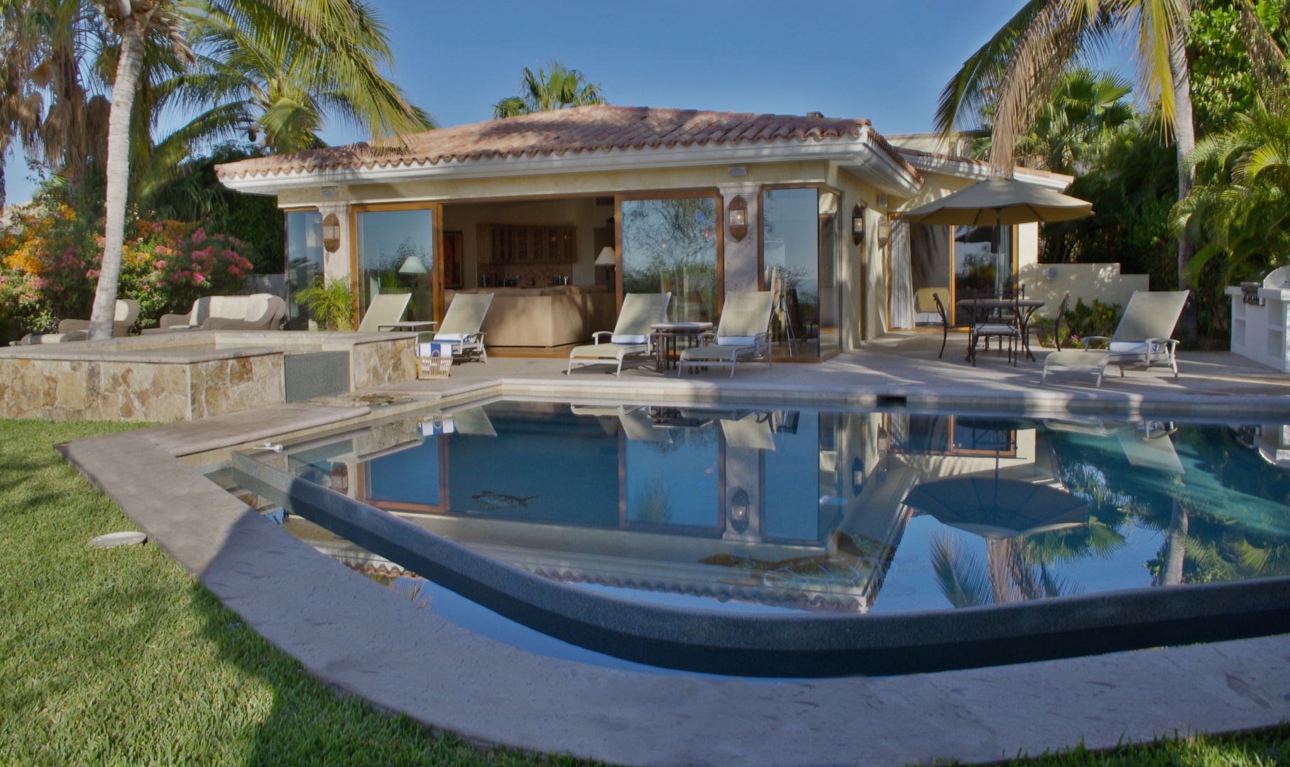 A tropical luxury villa framed by swaying palms, featuring a pristine pool and sun loungers where you can unwind under the warm sunshine in your own private paradise.