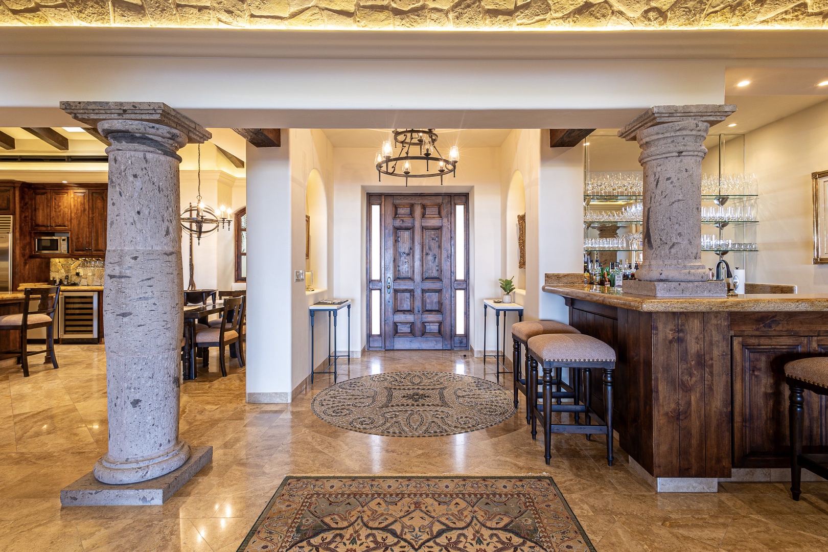 Grand entrance with stone columns and ornate chandelier welcomes you into this elegant space, where a handcrafted bar area awaits your evening gatherings.