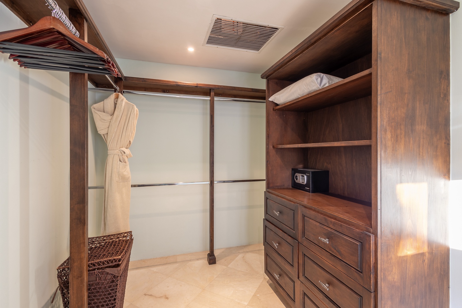A spacious walk-in closet features elegant wood shelving, hanging space for your wardrobe, a personal safe, and plush robes ready for your arrival.