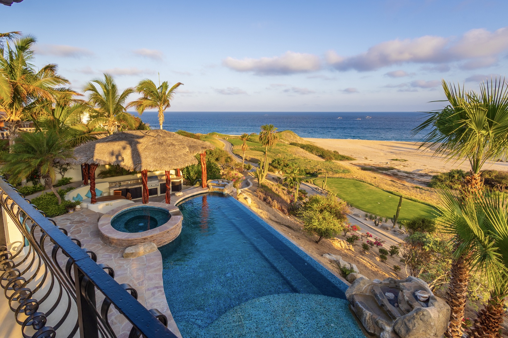 A beachfront oasis framed by swaying palms, showcasing a sparkling pool, inviting hot tub, and shaded outdoor lounge. The golden-hour light highlights direct beach access just beyond.