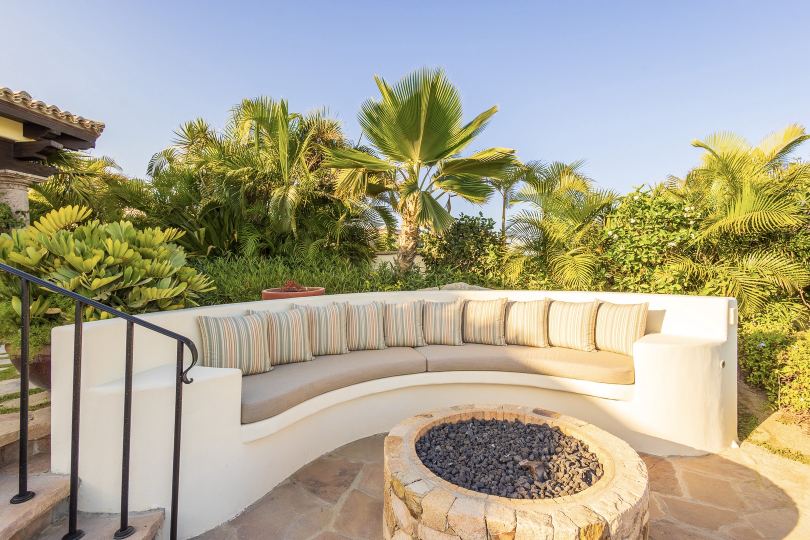 A curved outdoor seating area encircles a stone fire pit, framed by lush tropical palms—your ideal spot for starlit conversations and warm evenings together.