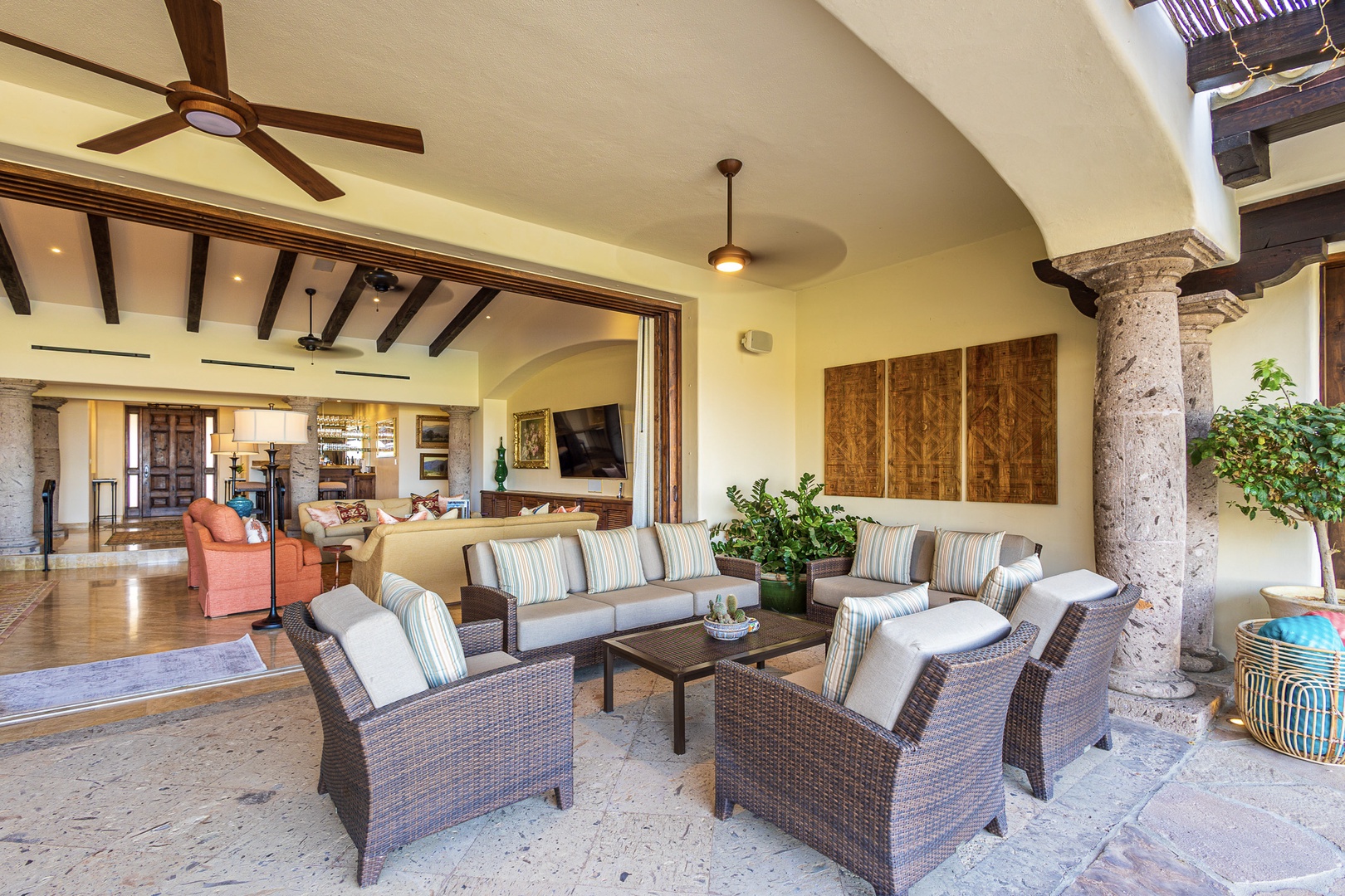 A spacious covered terrace seamlessly connects indoor elegance to outdoor relaxation, with plush seating inviting you to unwind while ceiling fans keep you cool under soaring vaulted ceilings.