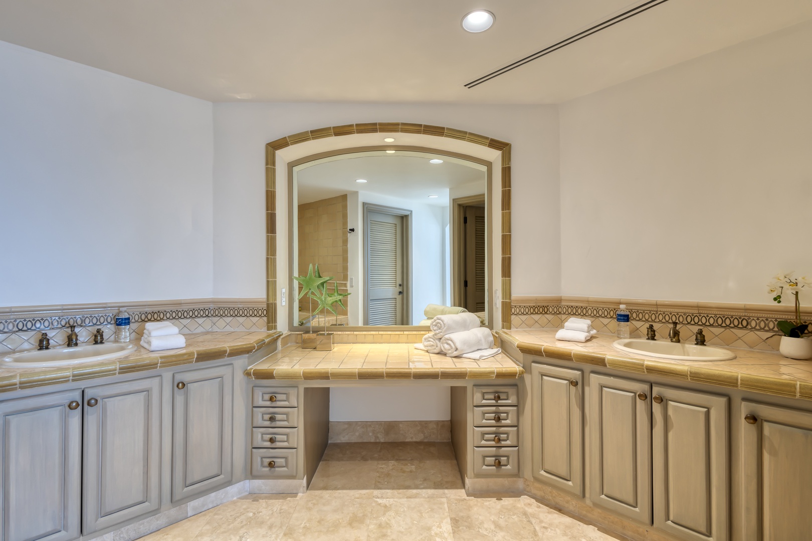 Your expansive dual-vanity bathroom features elegant tile countertops, ample storage, fresh towels, and a sophisticated arched mirror framing a private ensuite retreat.
