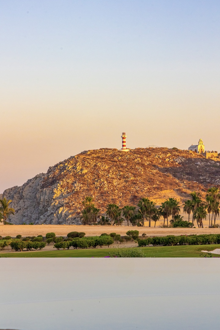 A distinctive lighthouse stands atop a rocky hillside, surrounded by palm trees and coastal landscapes visible from the property's scenic area.