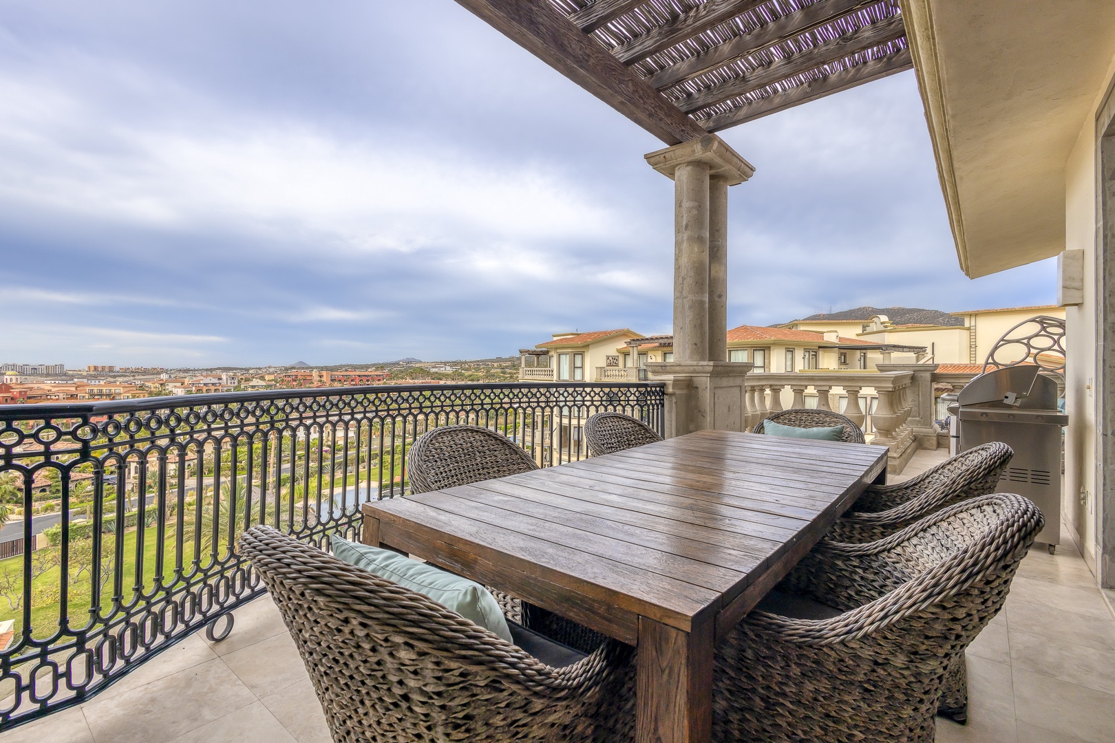 This spacious covered terrace offers scenic views across the area with a sturdy dining table and comfortable wicker chairs set up for outdoor meals in any weather.