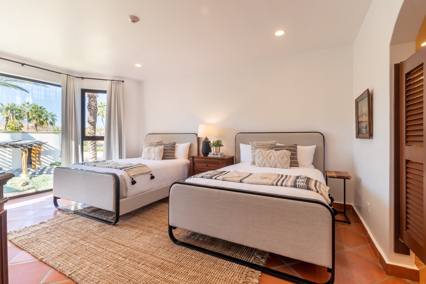 Your tranquil bedroom features two plush beds dressed in textured linens, tropical views through large windows, and warm tile floors. Unwind in this bright, airy space with subtle coastal touches.