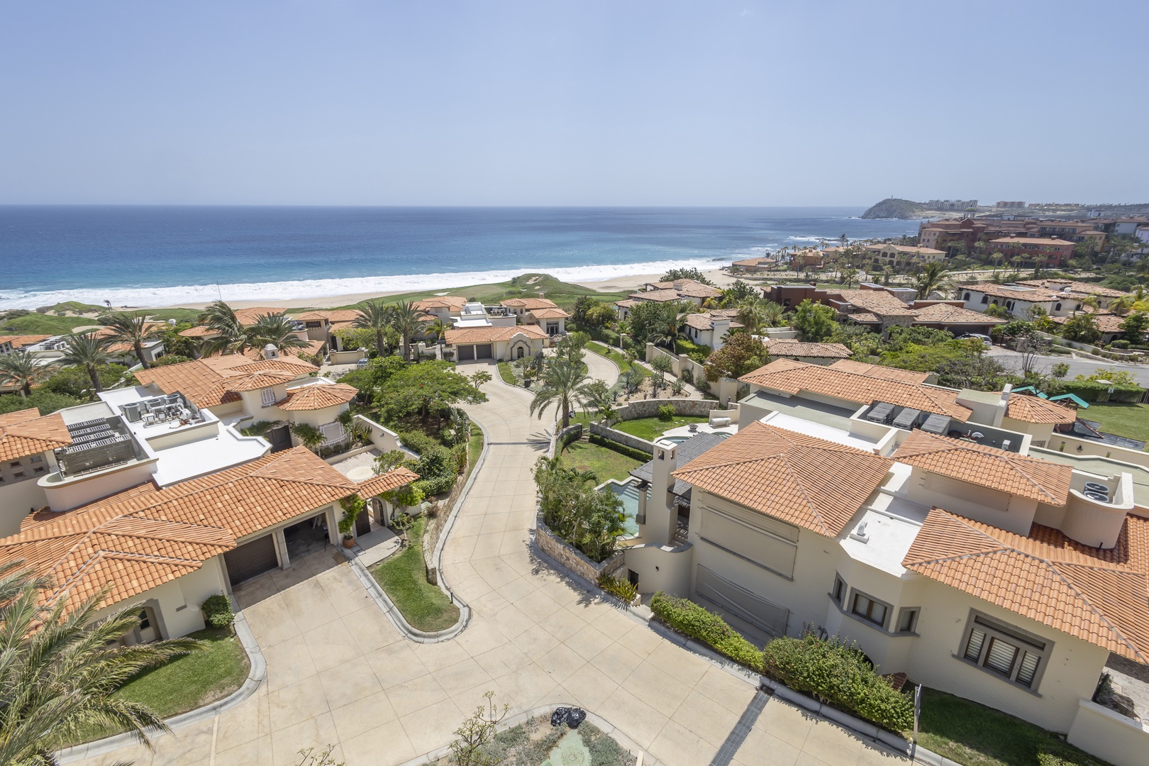 Oceanfront villa community featuring terracotta-roofed homes with private courtyards, lush gardens, and direct beach access along pristine shoreline with turquoise waters.