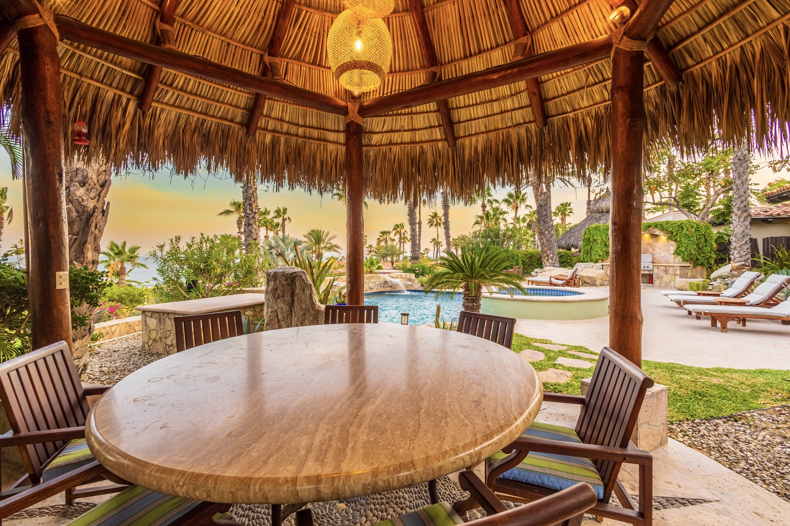 Gather under a palapa roof at your private outdoor dining table, where woven lanterns cast a warm glow over meals with friends and family. Beyond, your pool sparkles beneath swaying palms and ocean views.