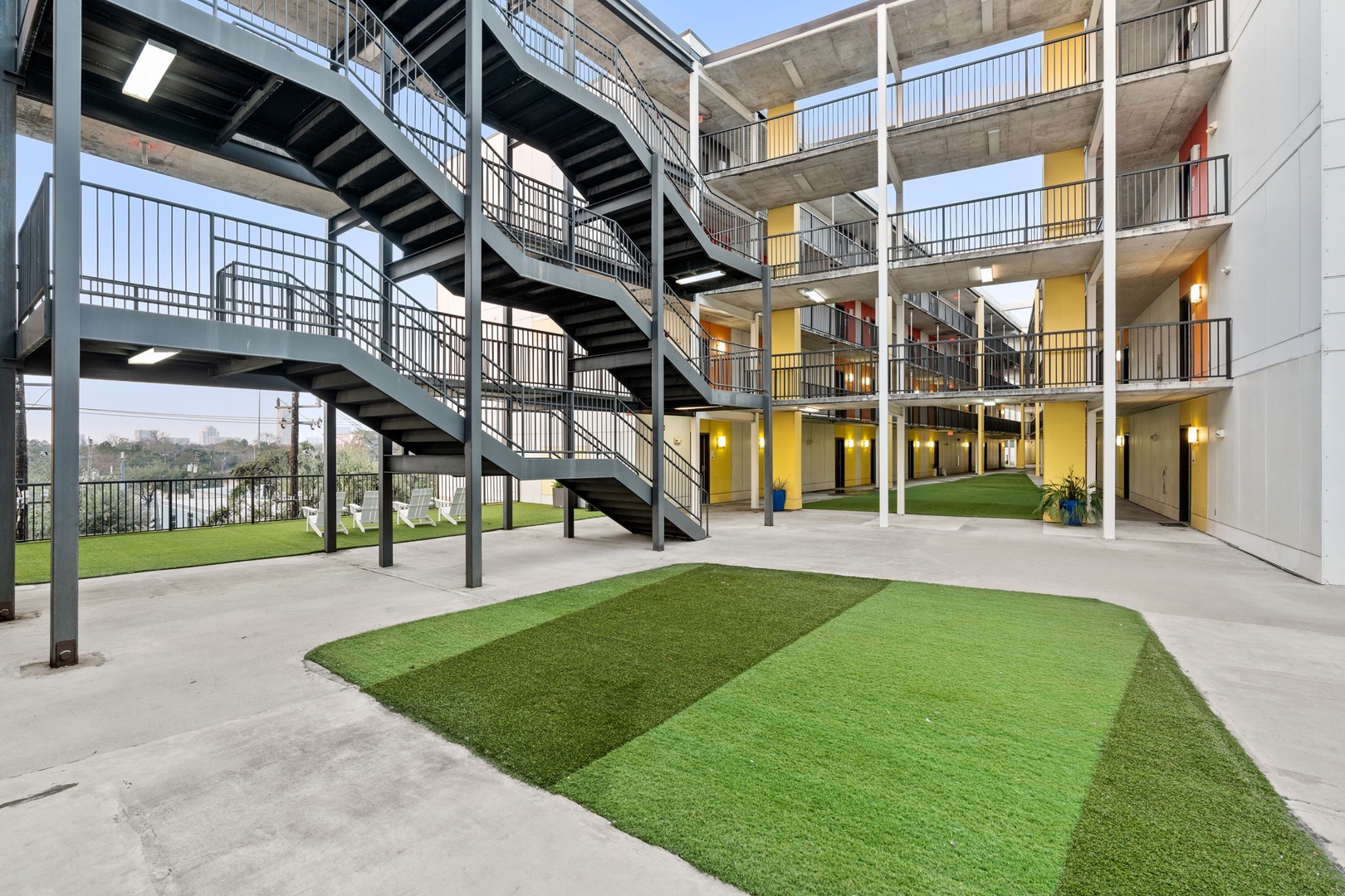 Modern apartment complex featuring multi-level concrete and steel construction with geometric green lawn spaces in the central courtyard area.