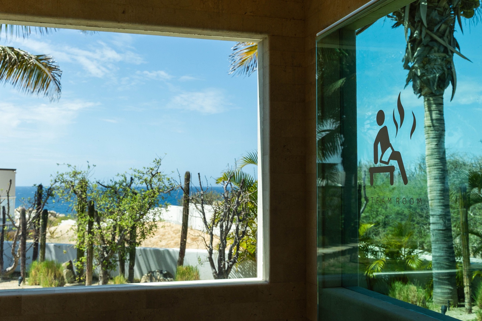 This coastal property features a steam room with tropical landscaping and ocean glimpses visible through the windows, situated in a tranquil beachside setting.