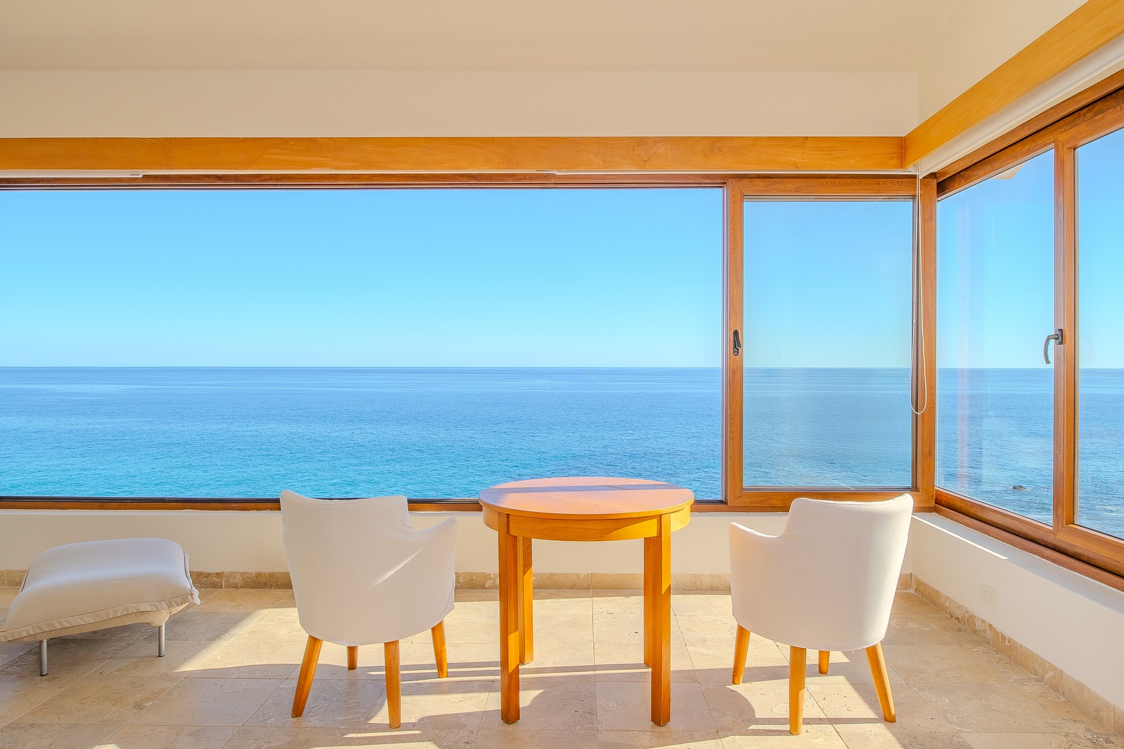 Relax in your sunlit seating area with floor-to-ceiling windows framing endless ocean vistas. Sip morning coffee at the cozy table as gentle light fills the space.