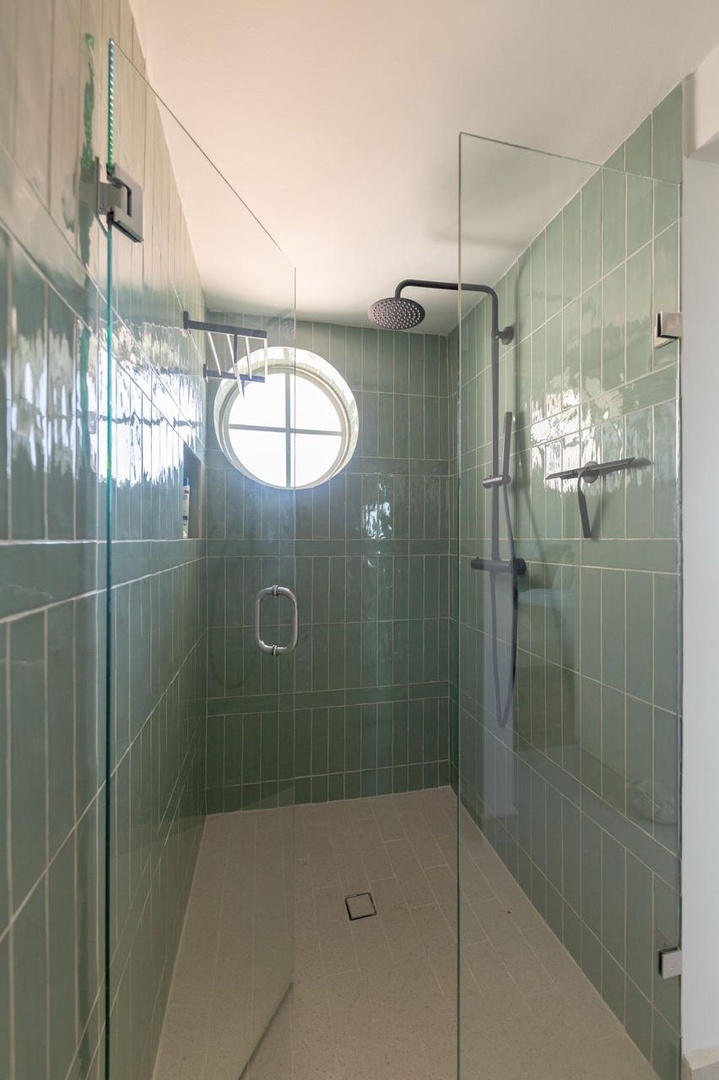 Step into your modern glass-enclosed shower with soothing green tile and rainfall showerhead for a refreshing, spa-like experience.