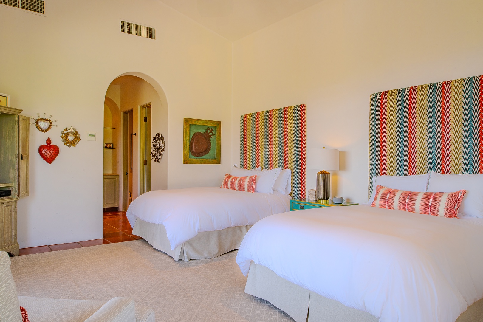 Unwind in your bright, cheerful bedroom with two plush beds dressed in crisp linens and vibrant patterned headboards that add personality to your space. Charming decor and soothing earth tones create warmth.