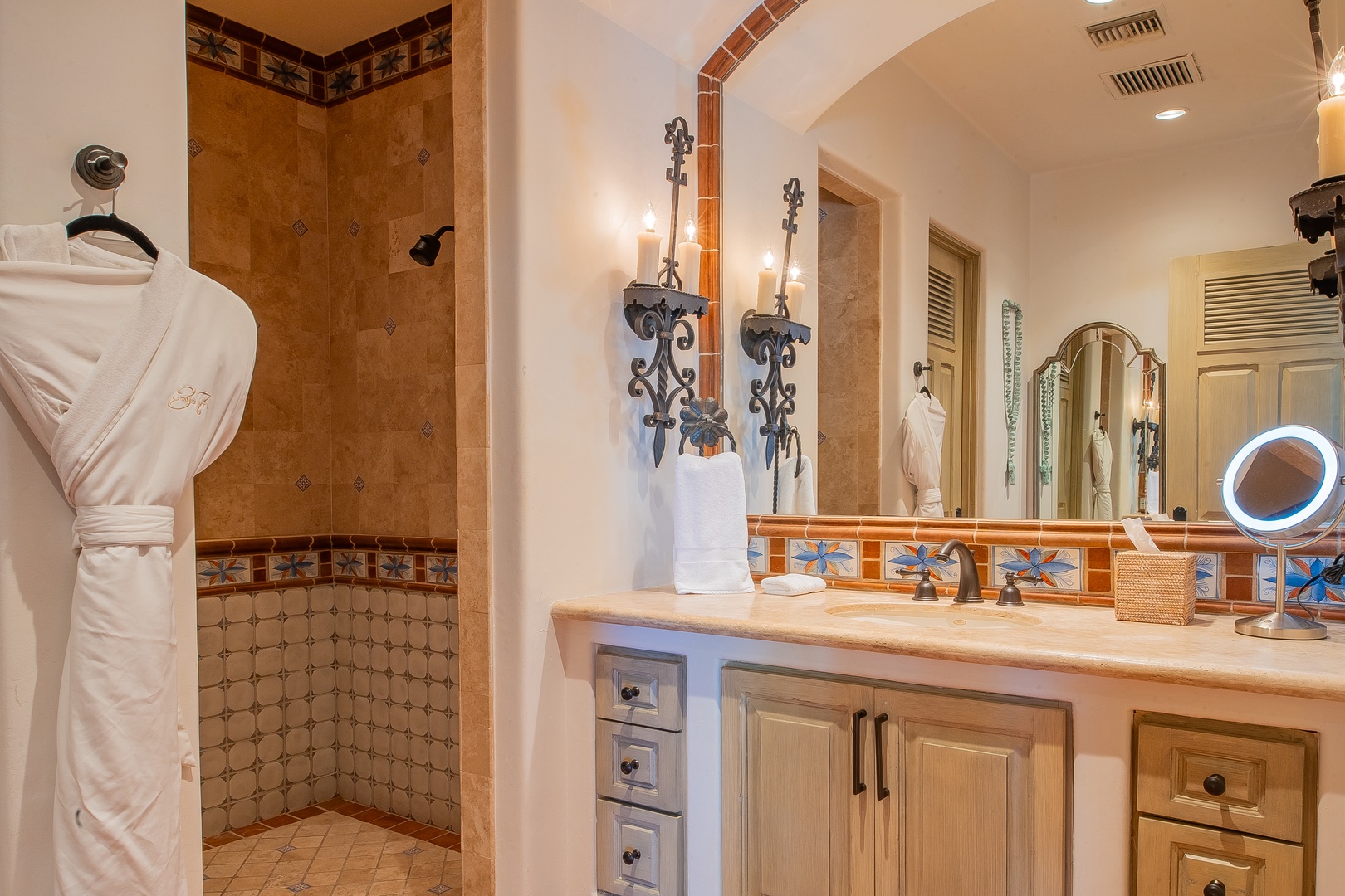 Your elegant bathroom features a spacious walk-in shower with decorative tilework, a well-appointed vanity, and plush robes awaiting your arrival for the ultimate comfort.