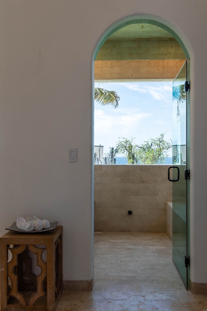Step through this arched doorway into a serene open-air shower where coastal breezes and blue skies transform your daily ritual into a tropical escape.