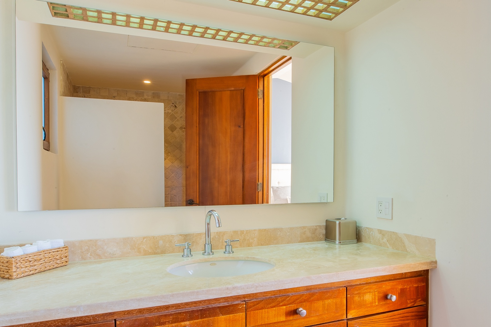 Fresh towels await you in this bright bathroom with warm wood cabinetry, polished stone counters, and a skylight that fills the space with natural light.