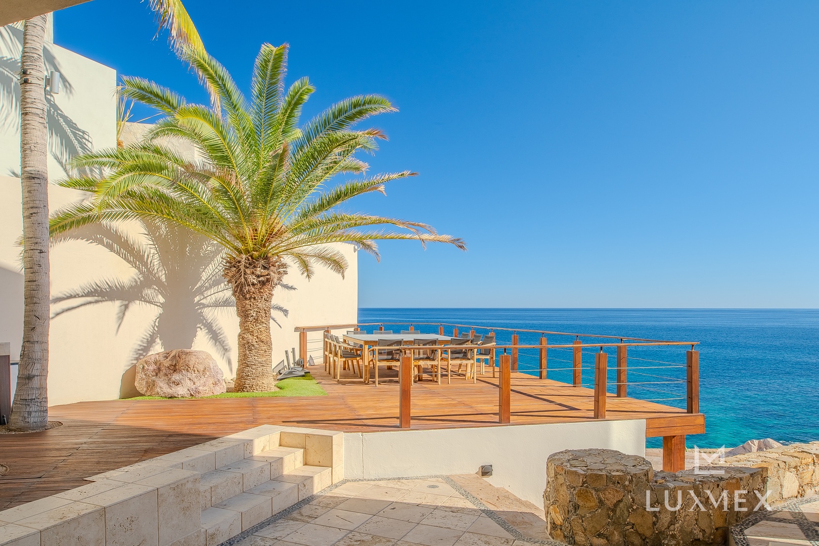 Stunning oceanfront terrace with wooden deck overlooking crystal-clear waters under endless blue skies.