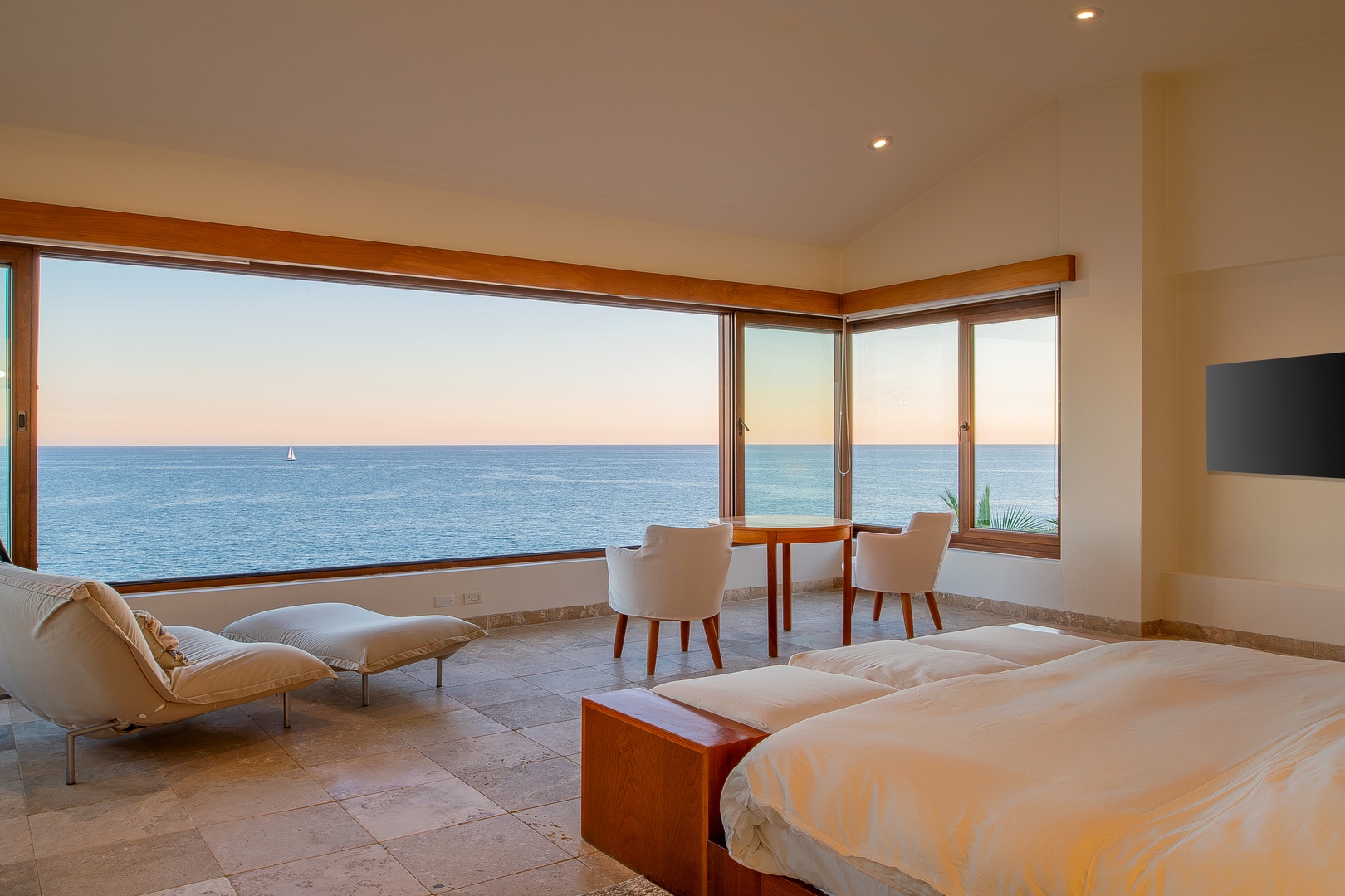 Drift off to sleep as the gentle sound of waves fills your spacious bedroom, where floor-to-ceiling windows frame endless ocean views and a cozy seating area invites quiet moments.