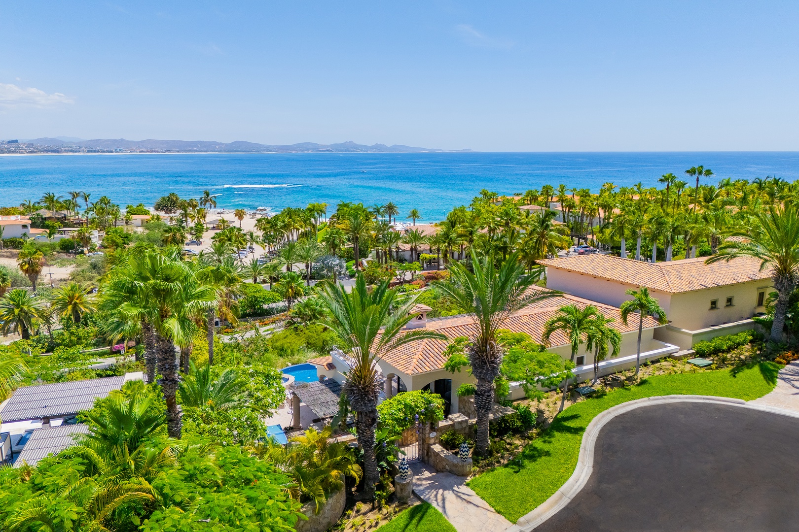 Aerial view of a beachfront property with lush tropical landscaping, private pool, and direct access to pristine turquoise waters and sandy shores.