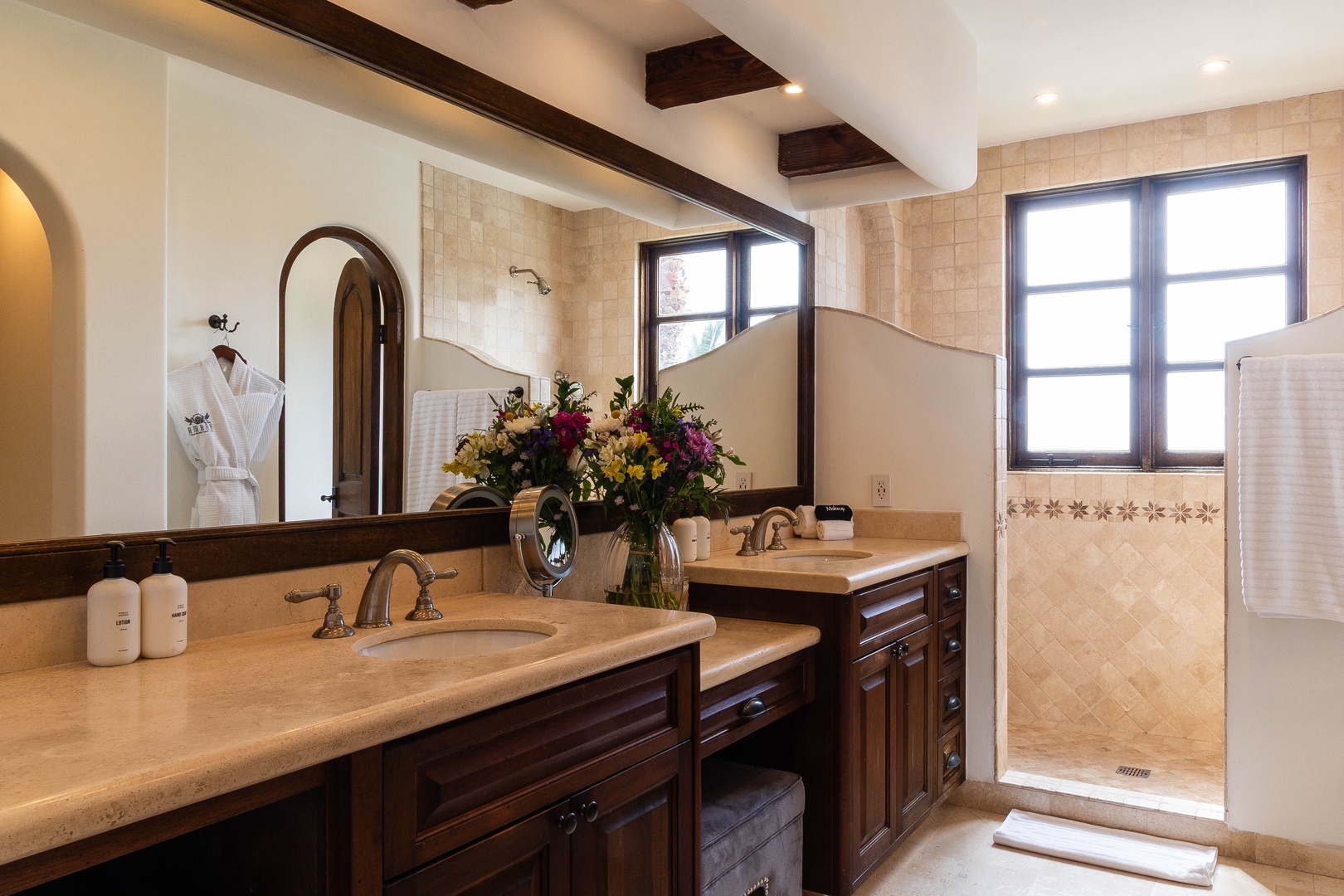 Step into your elegant ensuite bathroom with dual vanities, elegant archways, and a walk-in shower framed by natural light. Fresh flowers and plush robes await your arrival.