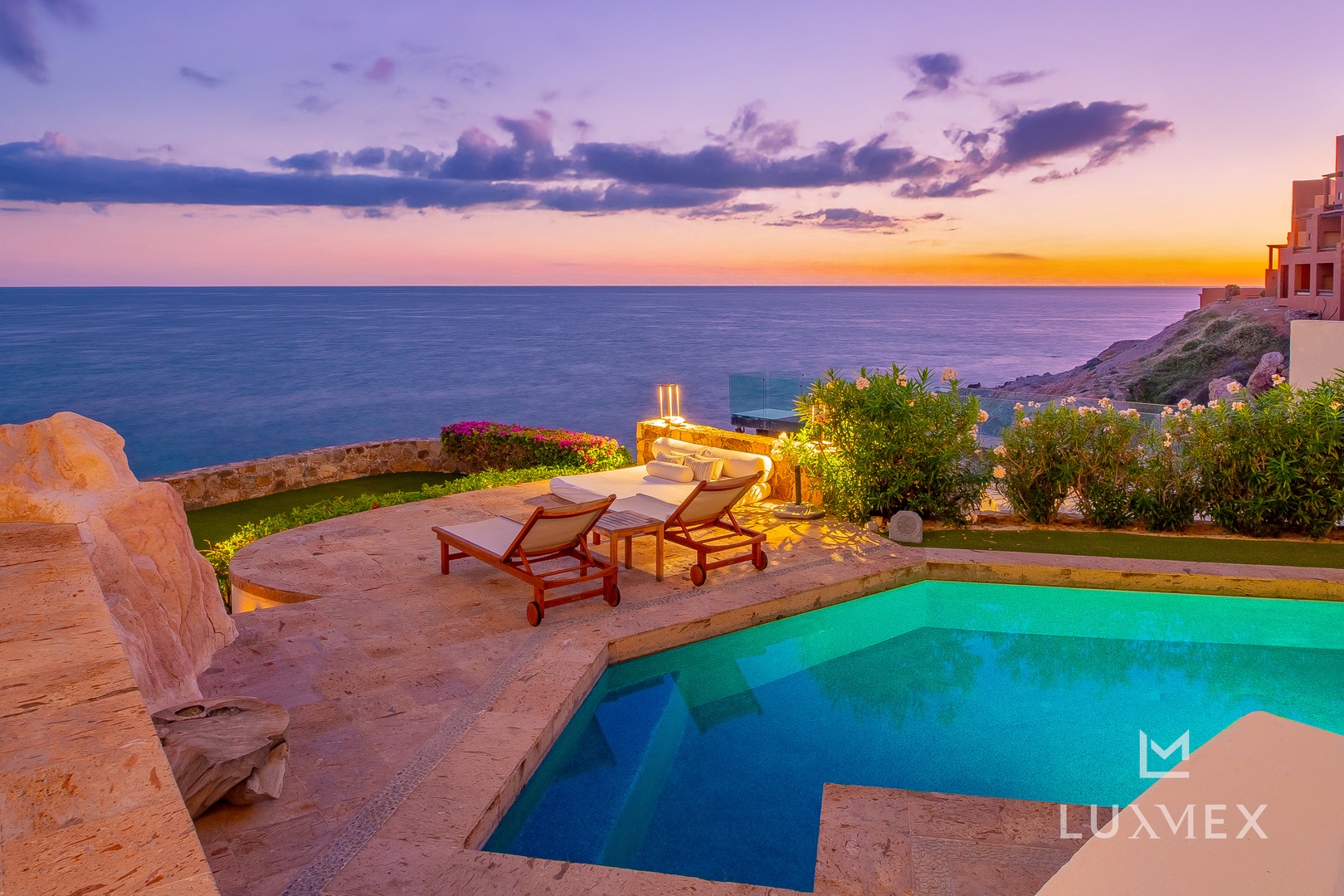 Stunning coastal villa with infinity pool overlooking the ocean at sunset, featuring outdoor loungers and manicured gardens.