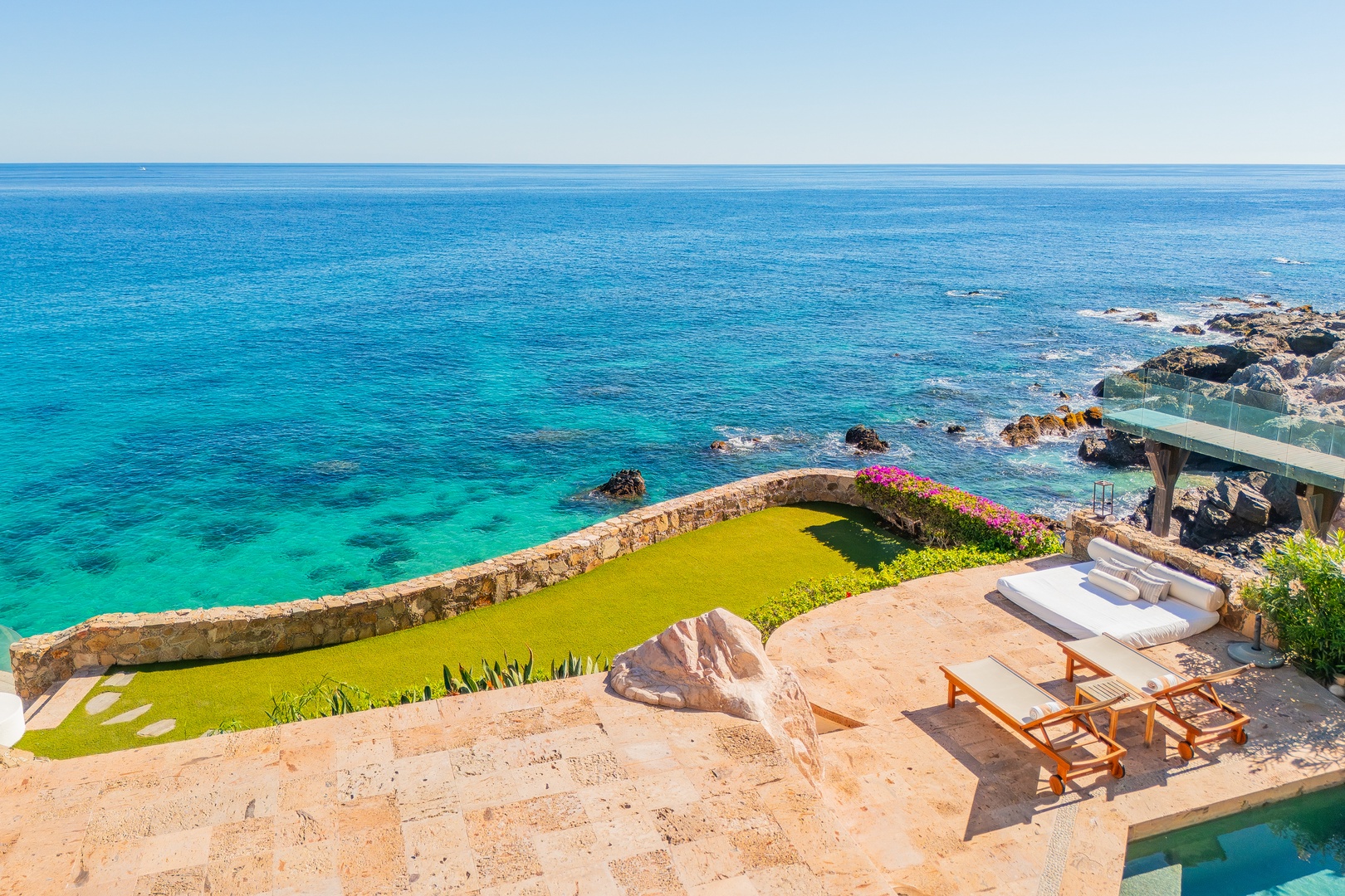 The property sits right on the coastline, offering direct access to crystal-clear turquoise waters, a manicured lawn, private terrace with lounge chairs, and stunning uninterrupted ocean vistas.