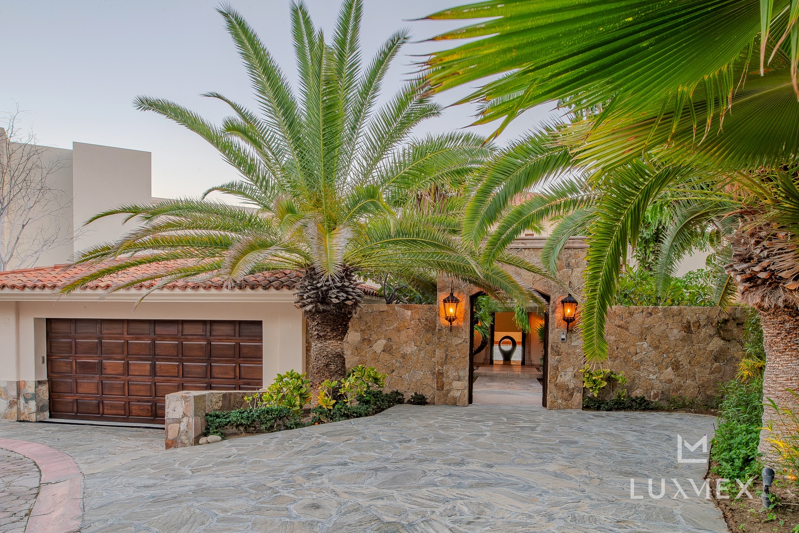 Stone entrance courtyard with tropical palms and warm lantern lighting creates a welcoming arrival experience.