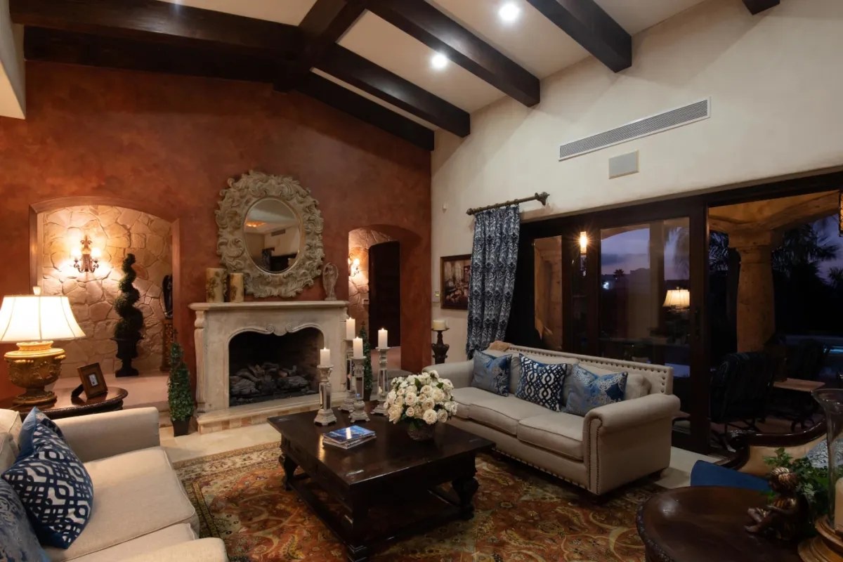 Unwind in your elegant living room with vaulted ceilings, exposed beams, a charming fireplace, and comfortable seating. Large windows frame peaceful evening views, creating the perfect retreat.