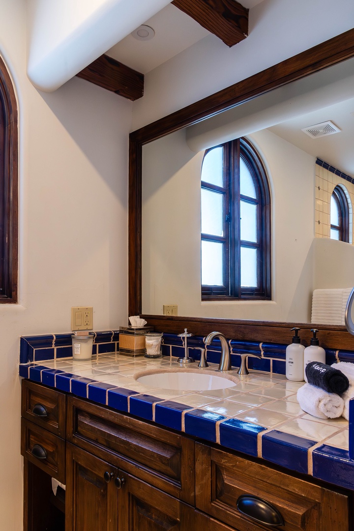 Elegant bathroom featuring deep blue handcrafted tile, exposed wooden beams, and arched windows that flood your private retreat with natural light.
