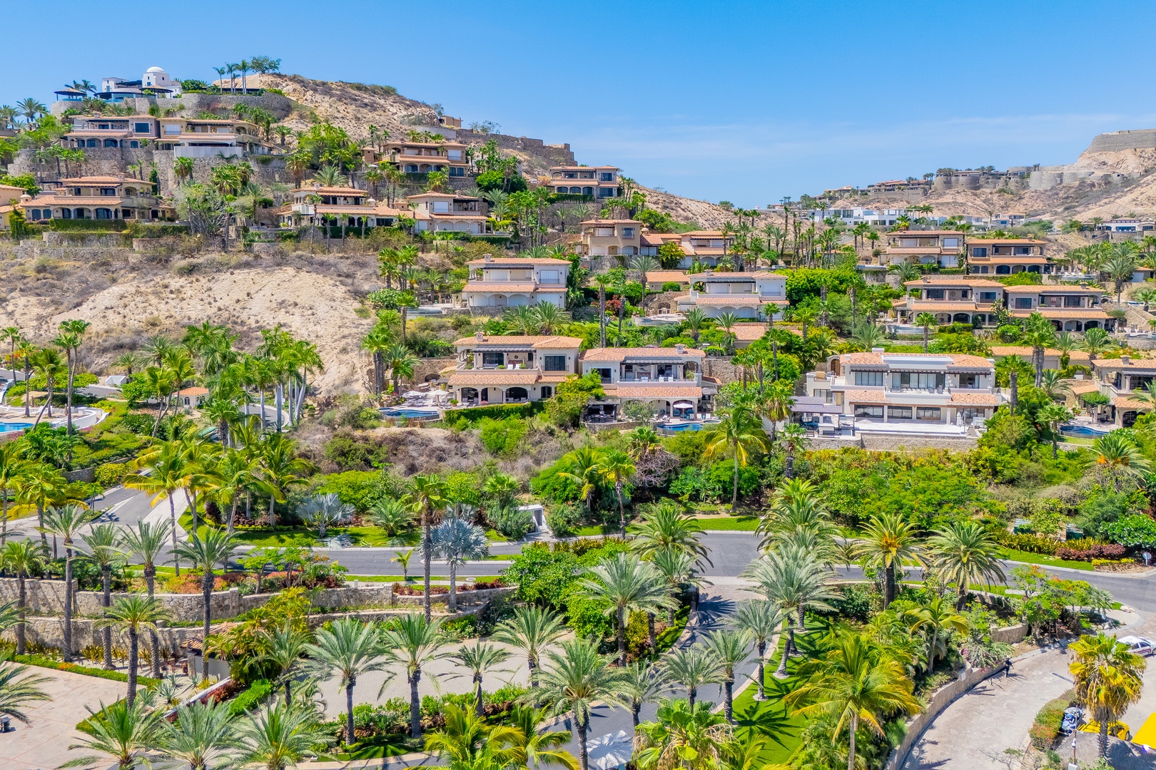 A hillside neighborhood featuring vacation homes nestled among lush tropical landscaping, with winding roads and pools dotting the scenic terrain under clear skies.