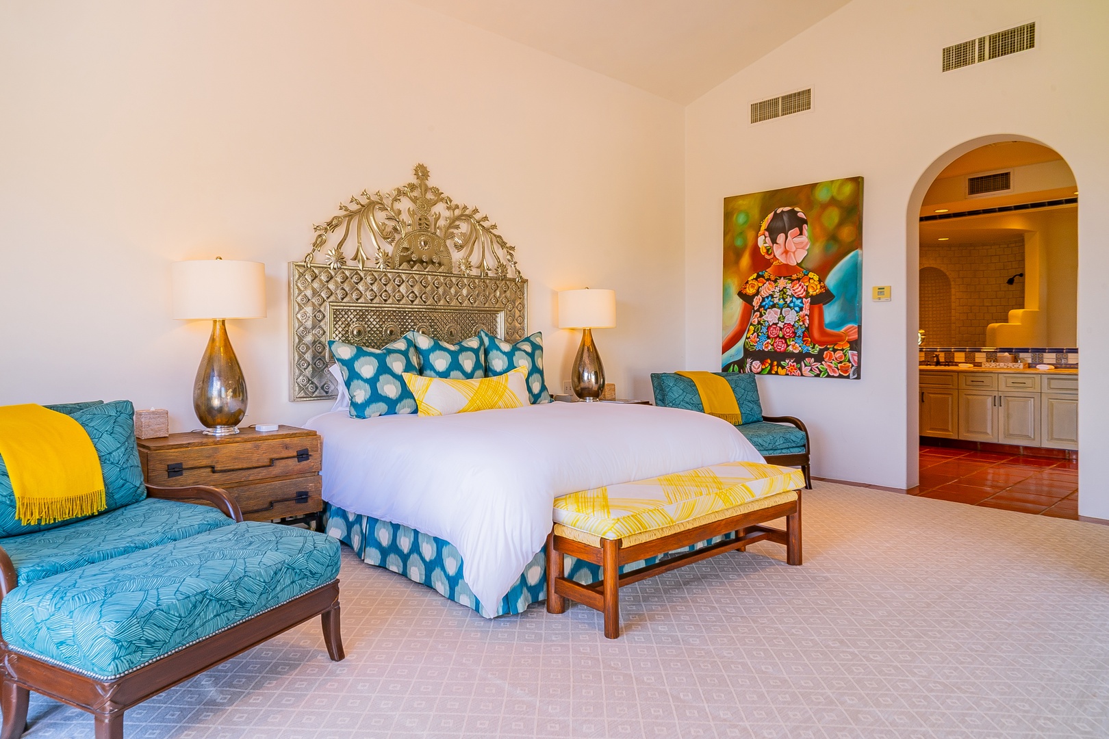 Slip into crisp white linens beneath an ornate headboard, surrounded by cheerful yellow and turquoise accents. Your private ensuite awaits through the elegant arched doorway.