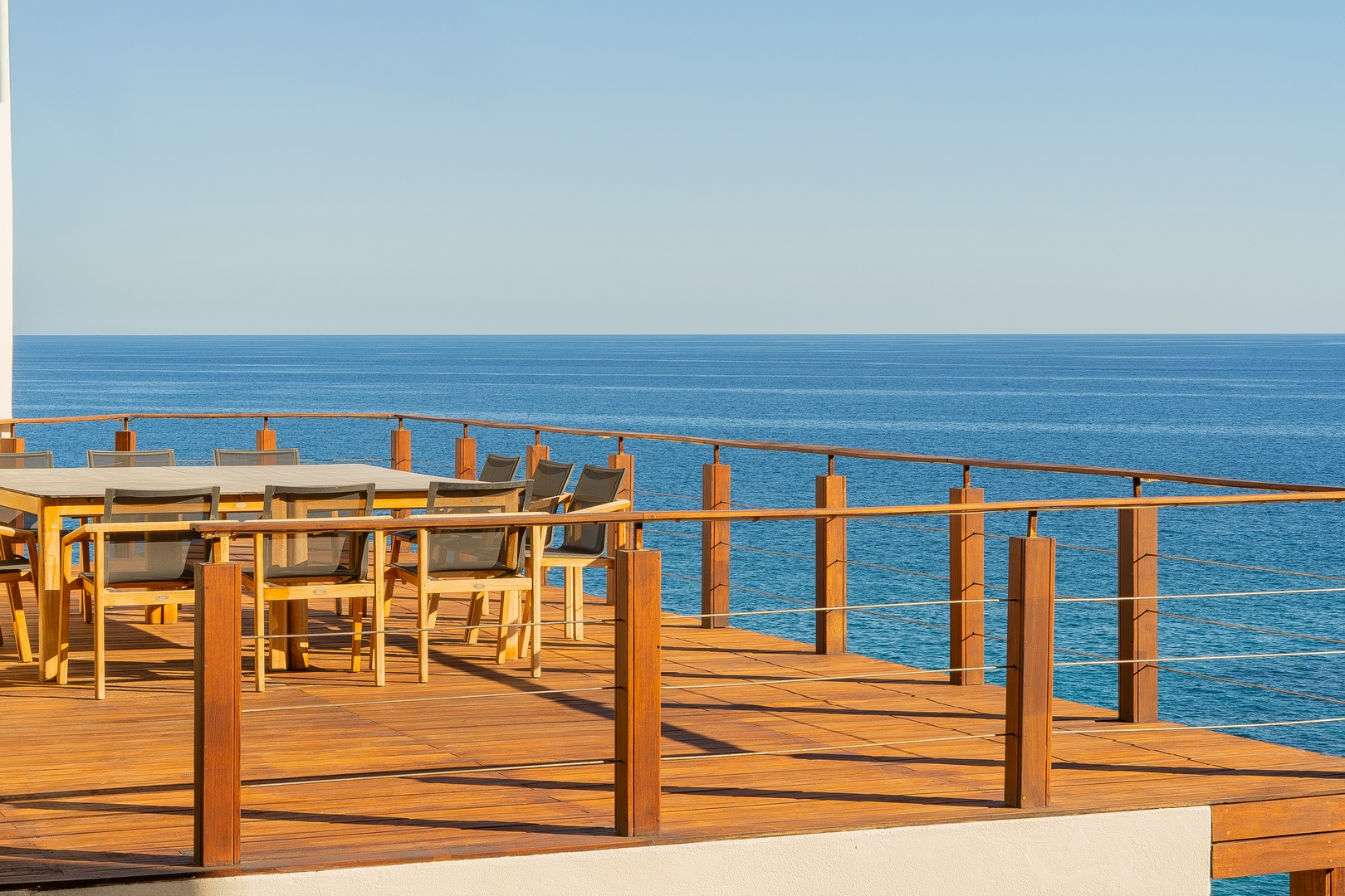 A stunning seaside terrace where you can dine with sweeping ocean views, framed by warm wooden decking and elegant glass railings that embrace the endless blue horizon.