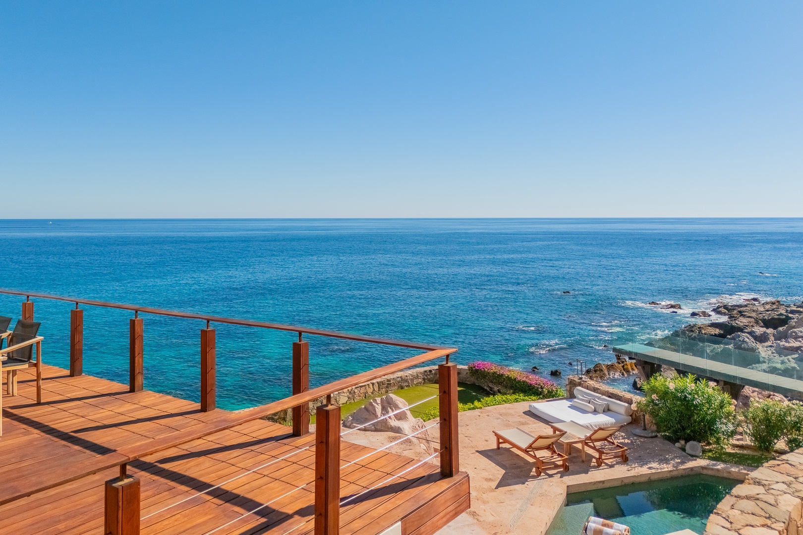 Oceanfront terrace with stunning coastal views, offering direct access to a private pool and sunbathing area surrounded by lush greenery and rocky shoreline.