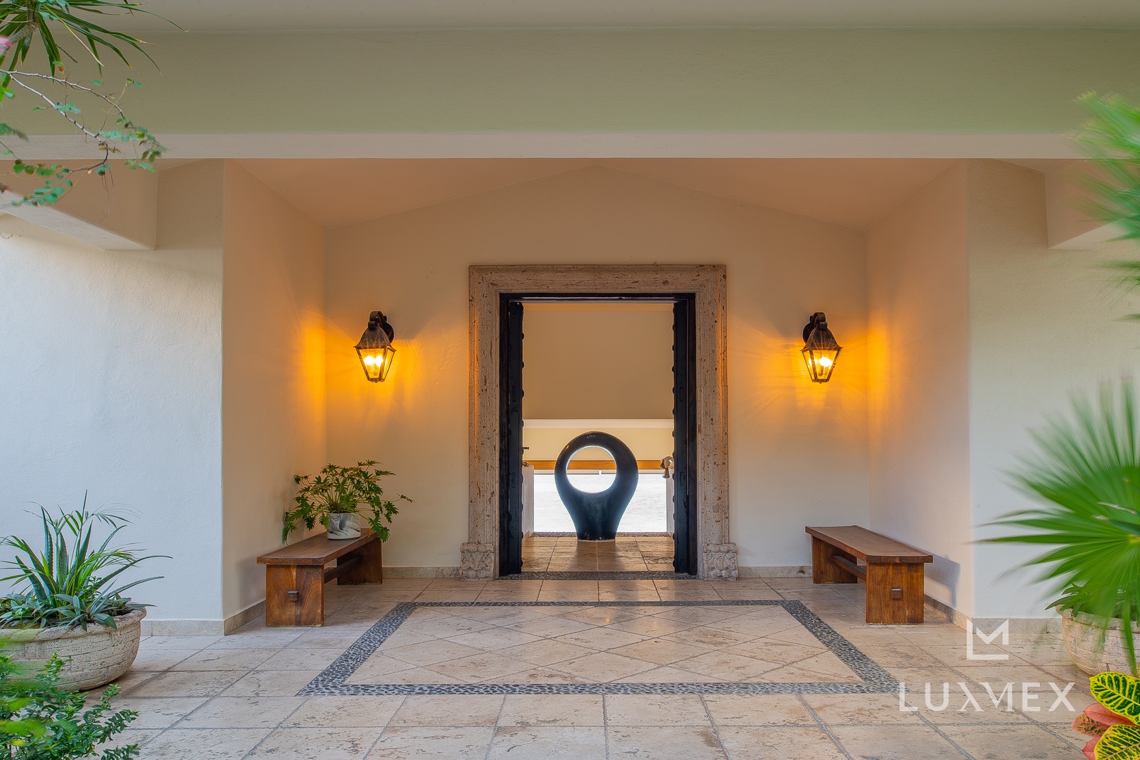 Warm lanterns illuminate your private entrance, where wooden benches and tropical plants create a serene welcome beneath soaring ceilings.