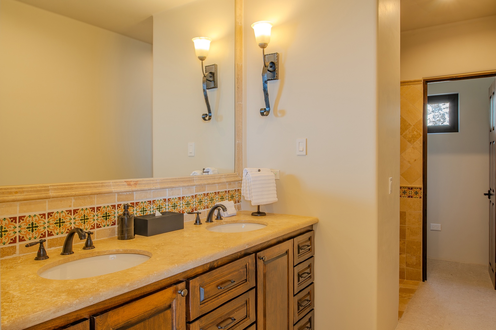 Luxurious dual vanity bathroom with warm wood cabinetry, decorative tile backsplash, and elegant sconce lighting creates your perfect morning routine space.
